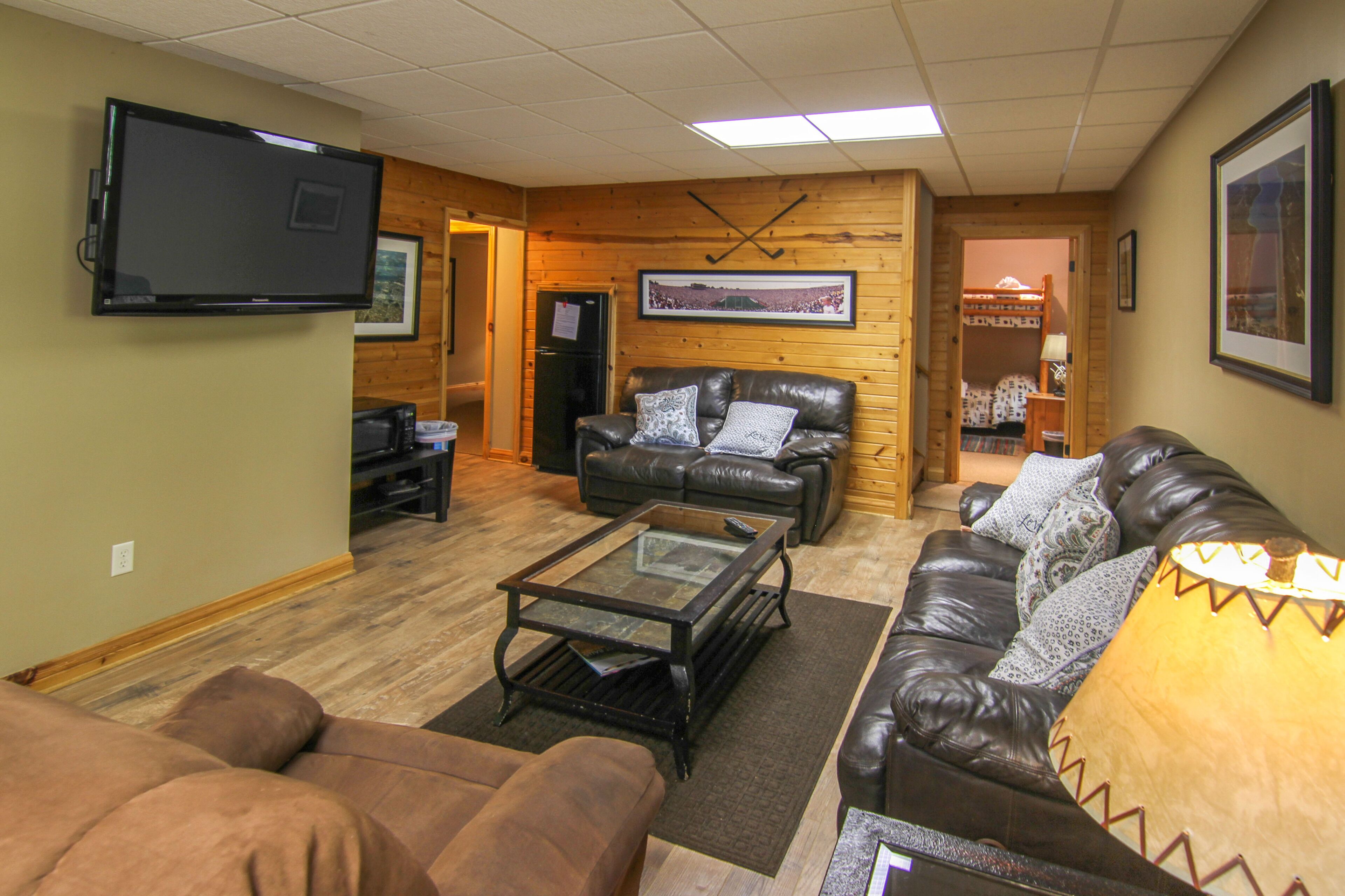 A living room with a television, leather couches, a coffee table, and a refrigerator.