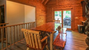 Interior de una cabaña de madera con una gran mesa de comedor, bancos y una chimenea de piedra.
