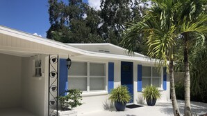 Un edificio blanco con contraventanas azules, un porche pequeño y plantas en macetas.