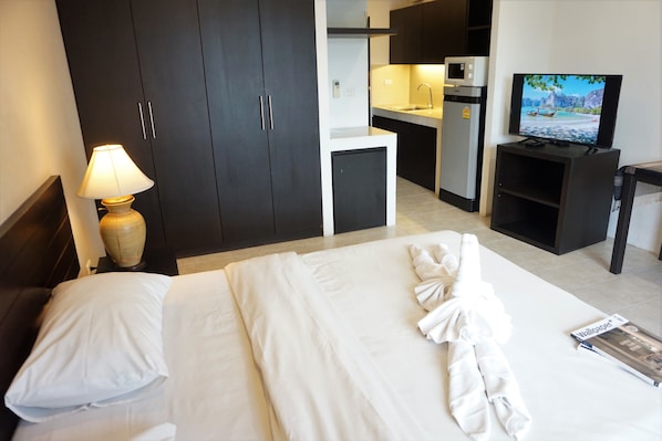 A hotel room with a bed, a TV, a desk, and a kitchenette.