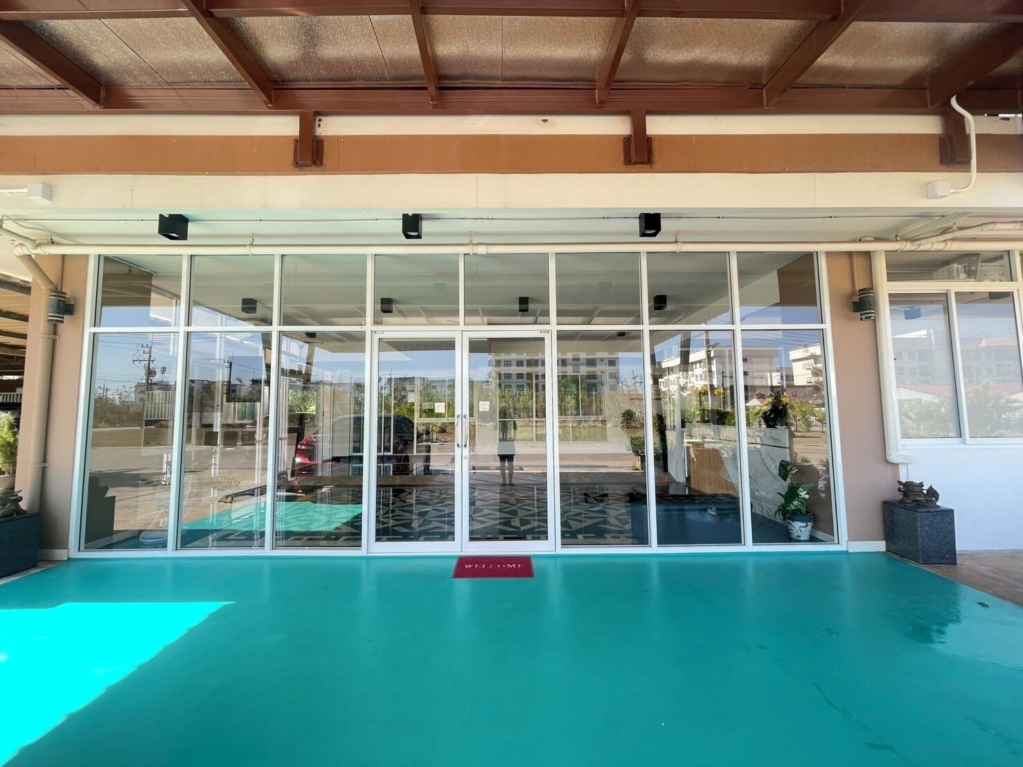 A swimming pool area with a glass enclosure, a red welcome mat, and a view of the street outside.
