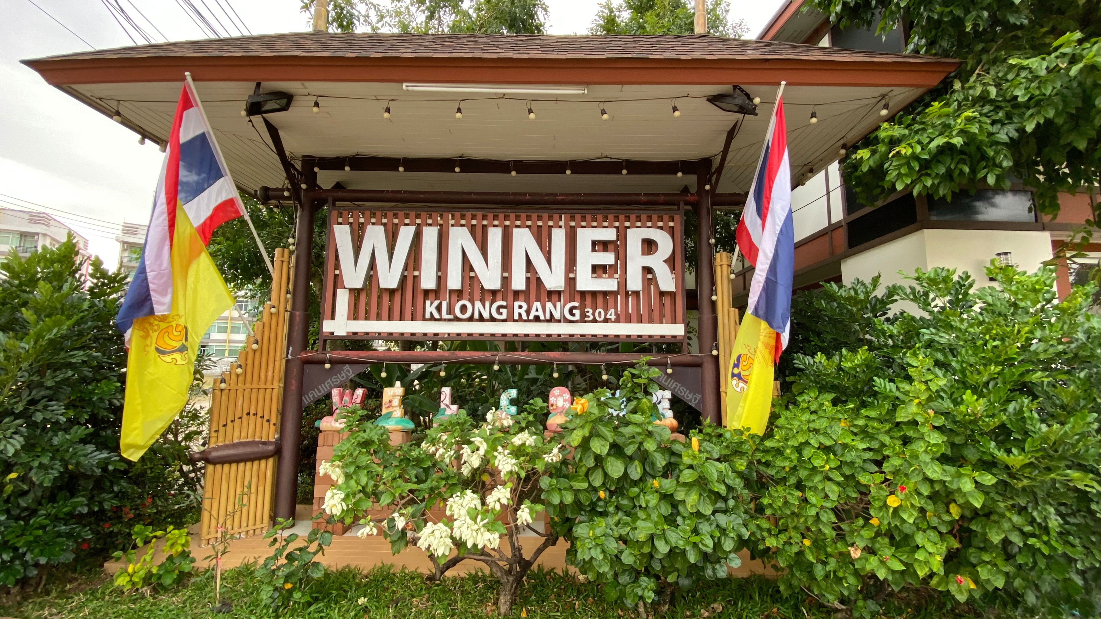 A sign reading "WINNER KLONG RANG 304" with flags and decorative elements.