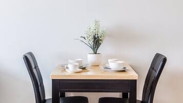 A dining table with two black chairs, a potted plant, and white cups and saucers on the table.