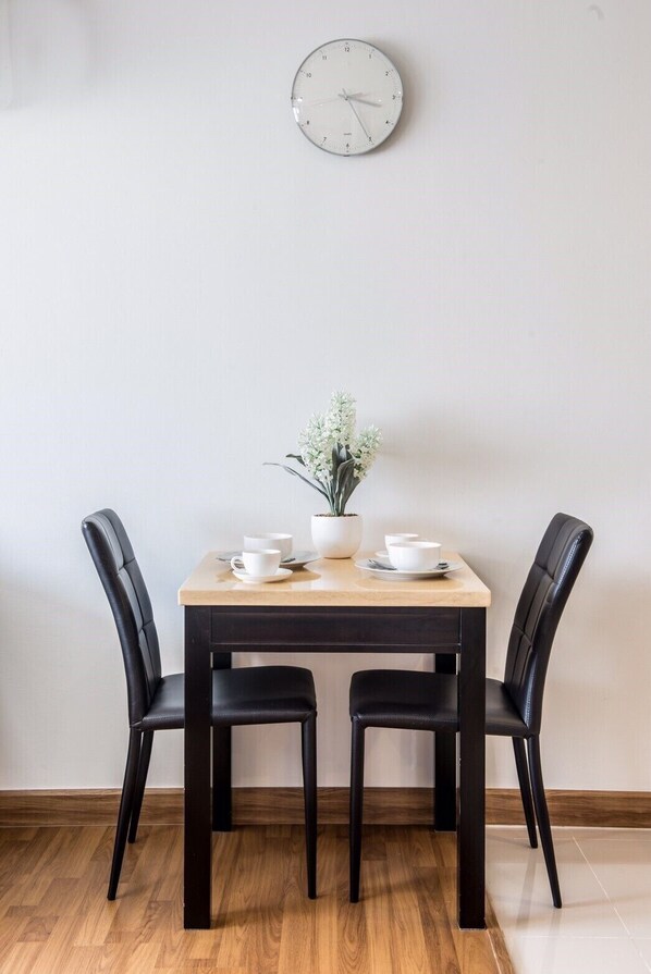 Une table à manger avec deux chaises noires, une plante en pot et des tasses et soucoupes blanches posées sur la table.