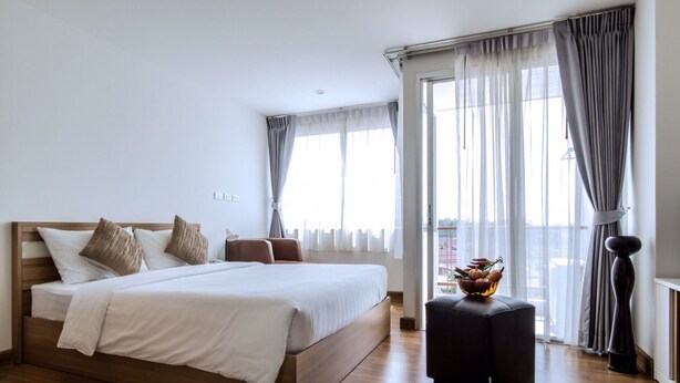 Een moderne hotelkamer met een groot bed, een klein tafeltje met een fruitschaal en een stadsgezicht door grote ramen.