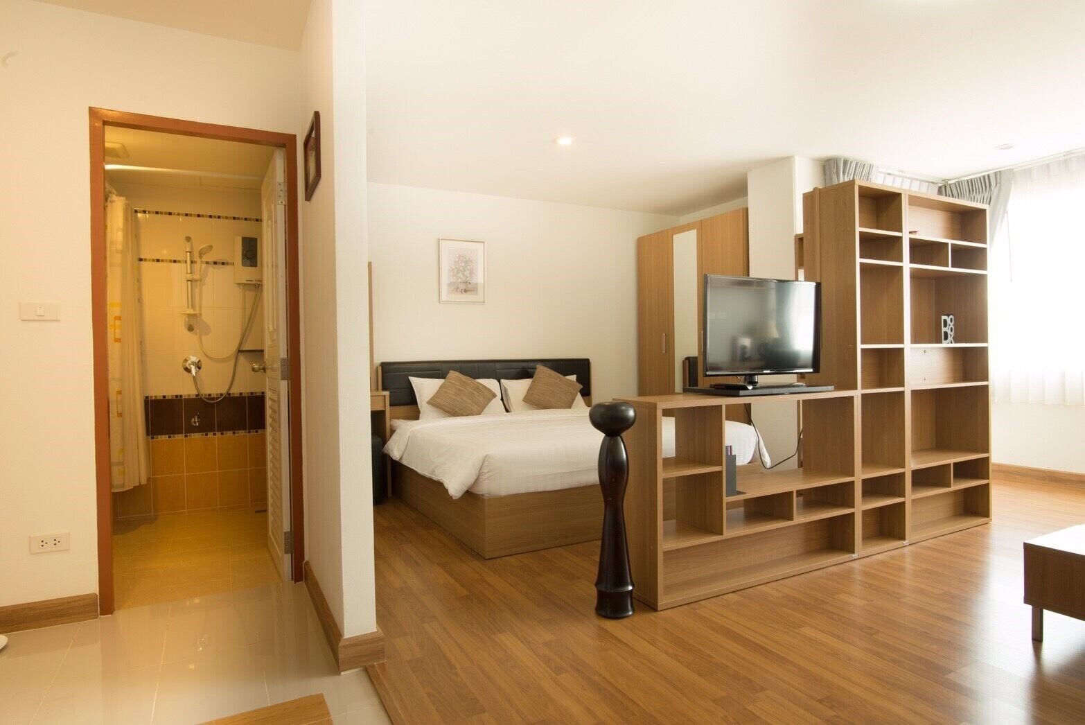 A modern hotel room with a bed, TV, wooden shelving, and a shower area.