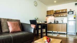 Een moderne woonkamer met een leren bank, een glazen salontafel met fruit, een eethoek met een stoel en een keuken met houten keukenkastjes en apparatuur.