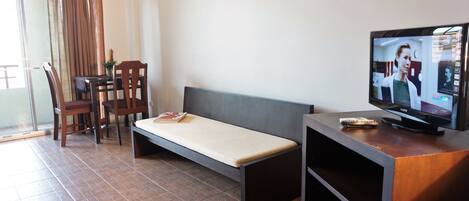A room with a bed, a TV, a table with chairs, and a window with curtains.