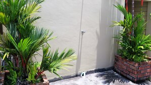 A corner of a building with a white wall, a metal showerhead, and potted plants. - Phompassorn Apartment (Chalong)