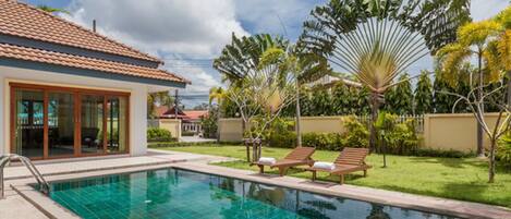 A swimming pool with tiled edges, surrounded by a lawn and palm trees.