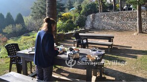 A picnic setup with a table, chairs, and a stone wall in a natural setting. - Shivapuri Village (Samundradevi)
