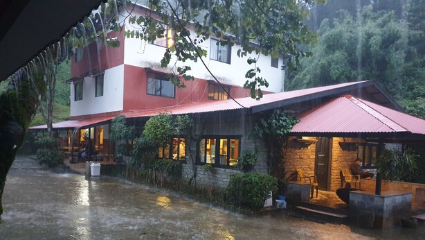 A building with a red roof and stone walls, featuring outdoor seating areas and a small water feature. - Shivapuri Village (Samundradevi)