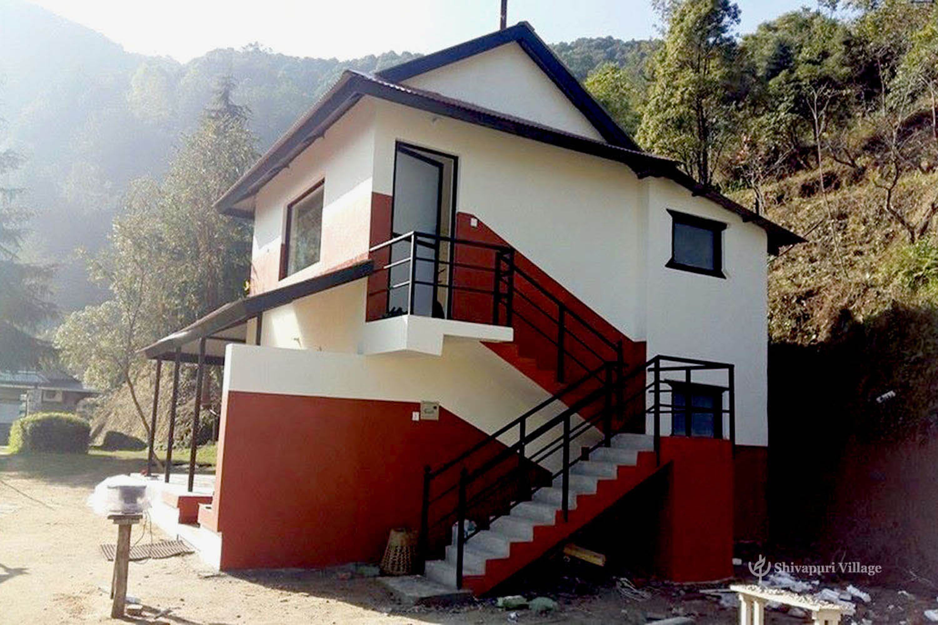 Un edificio de dos pisos con fachada roja y blanca, una escalera y un pequeño balcón.