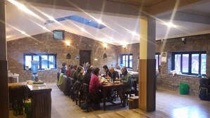 A dining area with wooden tables and chairs, stone walls, and large windows. - Shivapuri Village (Samundradevi)