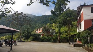 A paved driveway leading to a building with a red and white facade, surrounded by greenery and hills in the background. - Shivapuri Village (Samundradevi)