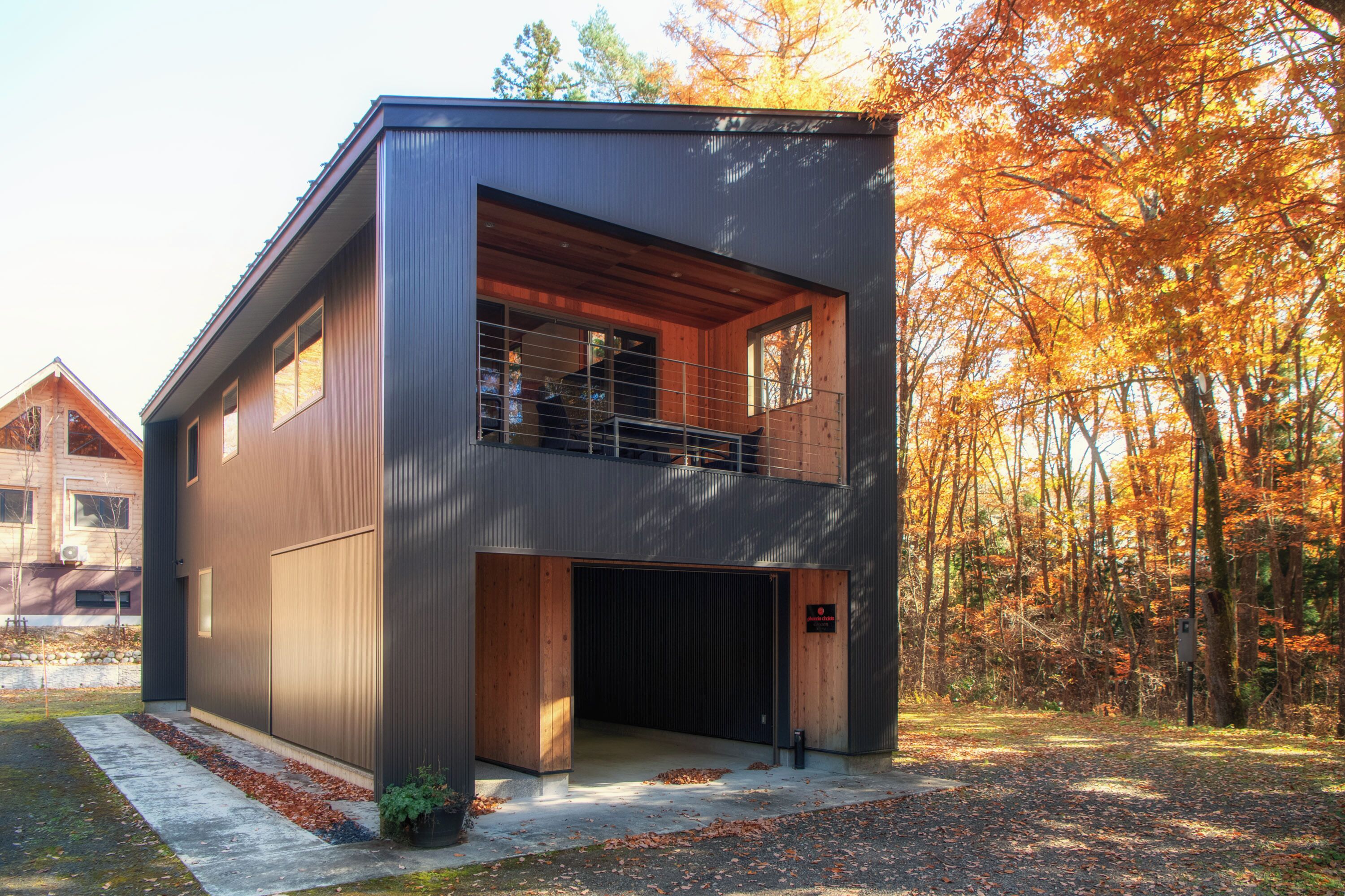 A modern two-story house with a garage, surrounded by autumn trees.