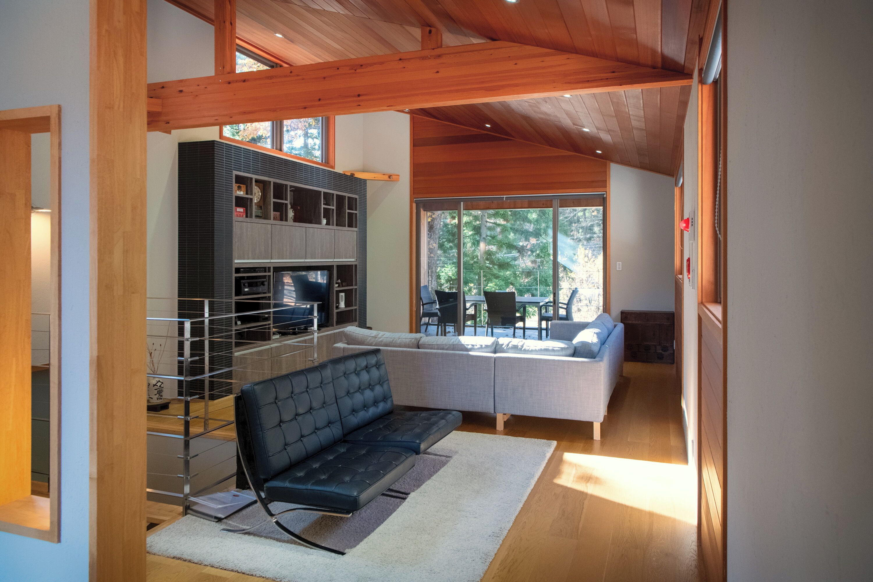 A modern living room with a black sofa, a grey sectional sofa, and a wooden ceiling.