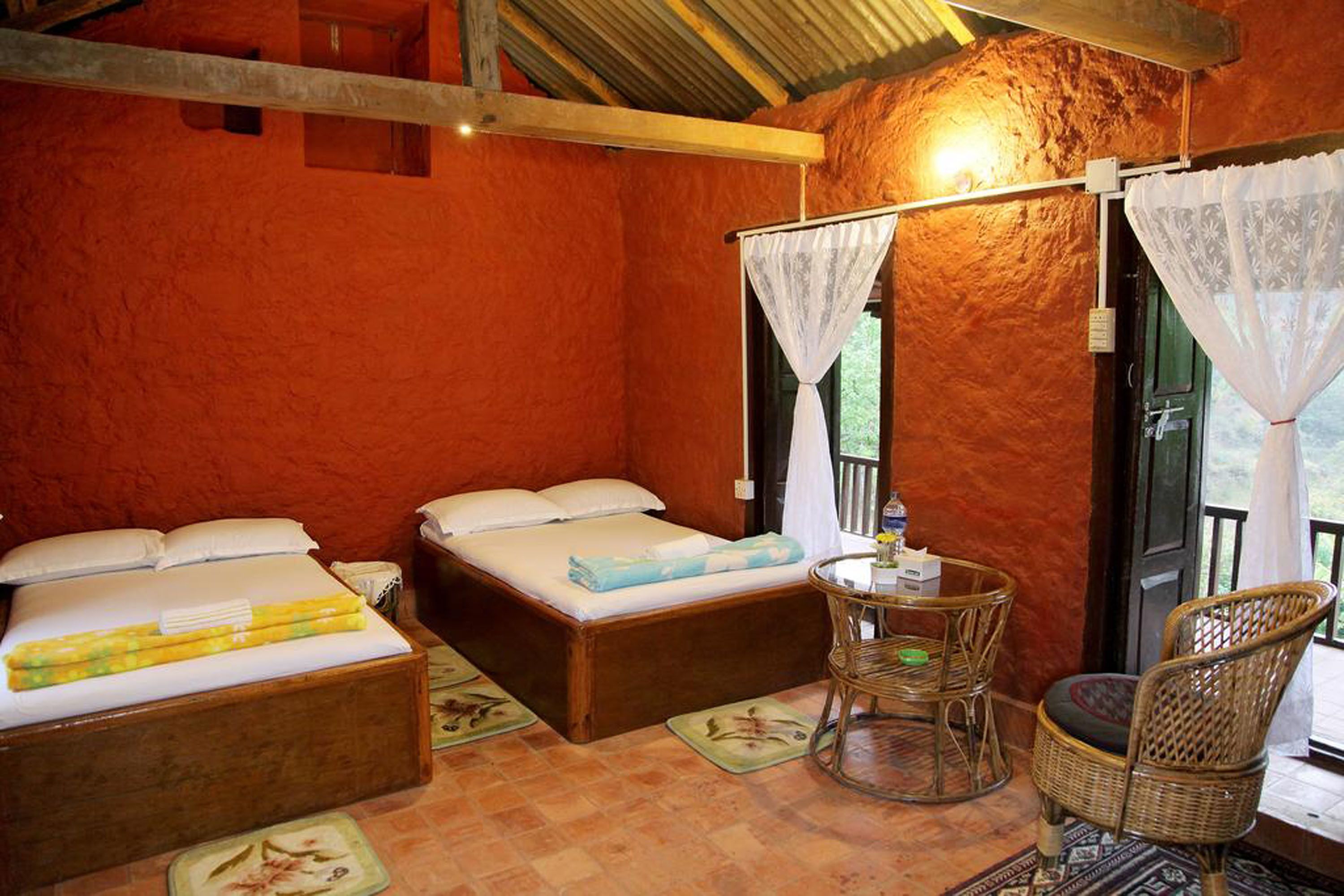 A room with two beds, a small table with a chair, and a window with a view.