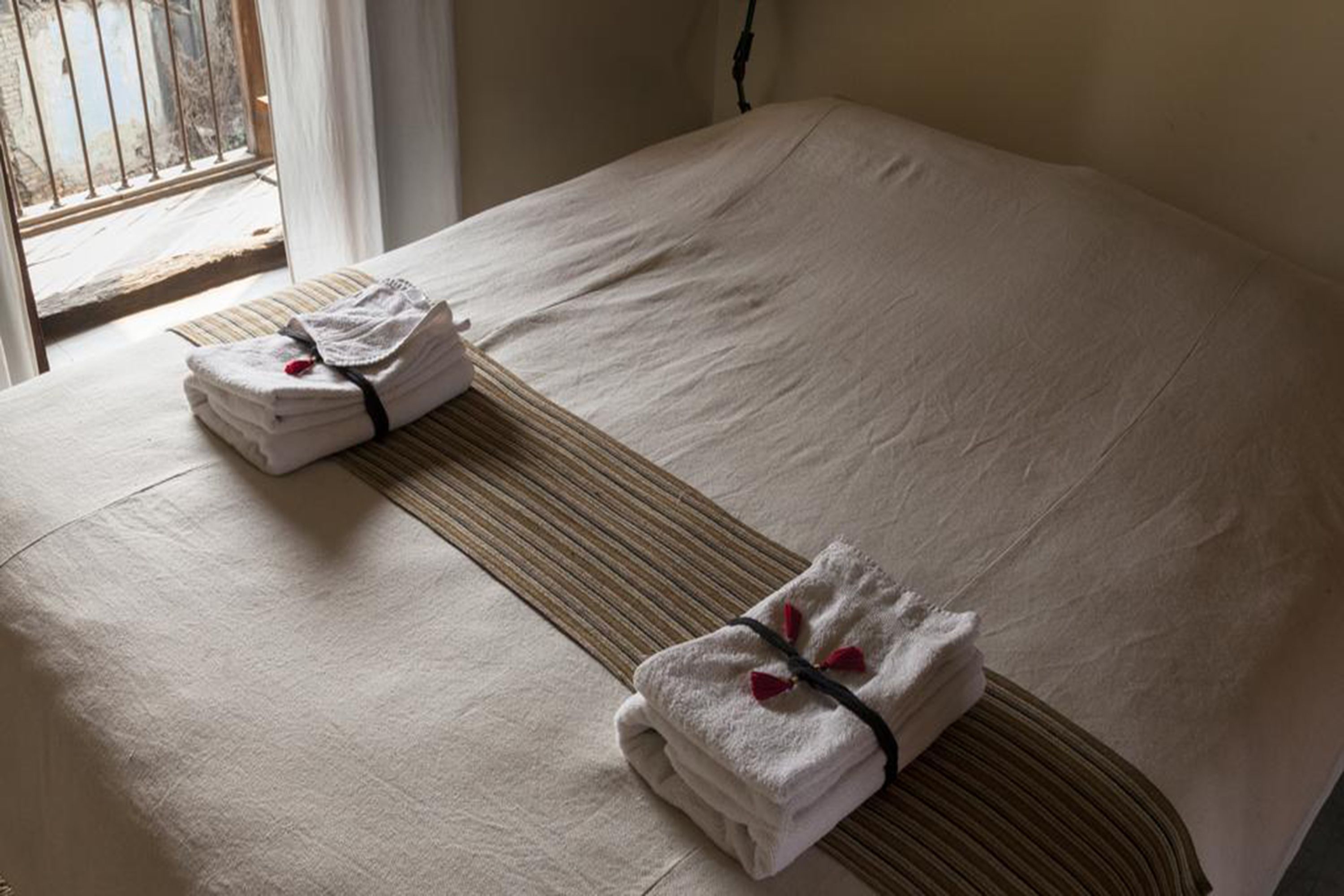 Una cama bien hecha con una toalla doblada y otra enrollada, y un cabecero de madera.
