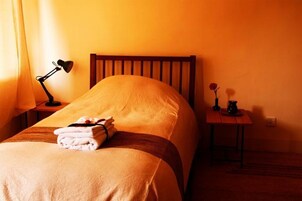 A neatly made bed with a wooden headboard, a bedside lamp, a small table with a vase of flowers, and a folded towel on the bed.
