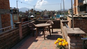 A rooftop terrace with a table and chairs, a flower arrangement, and a view of the cityscape and mountains in the background. - Hiranya Guest House (Lalitpur)