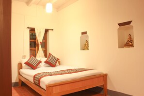 A wooden bed with a white mattress, two pillows, and a patterned blanket.