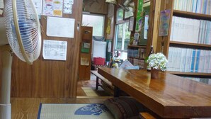 A cozy room with a wooden desk, a fan, a bookshelf, and various papers and notes on the walls. - Tomarigi - Hostel (Yakushima)