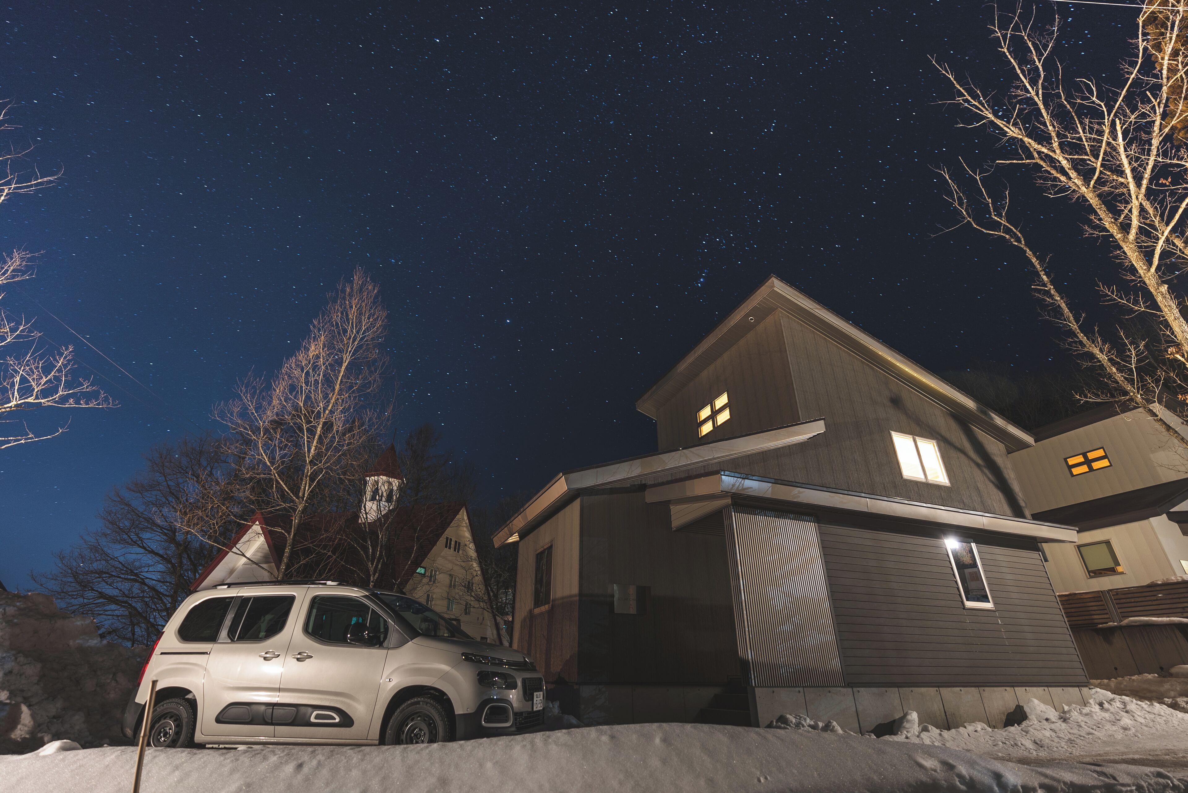 Una casa moderna con un coche estacionado adelante, rodeada de nieve.