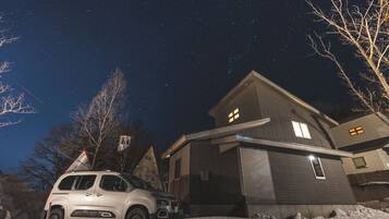 Una casa moderna con un coche estacionado adelante, rodeada de nieve.