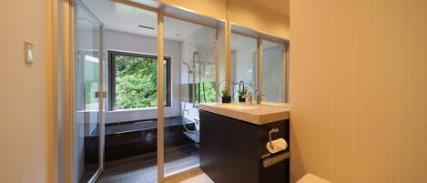 A modern bathroom with a glass shower enclosure, a toilet, and a sink with a towel dispenser.