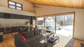 A modern living space with a kitchen, dining area, and a large window offering a view of a snowy landscape.