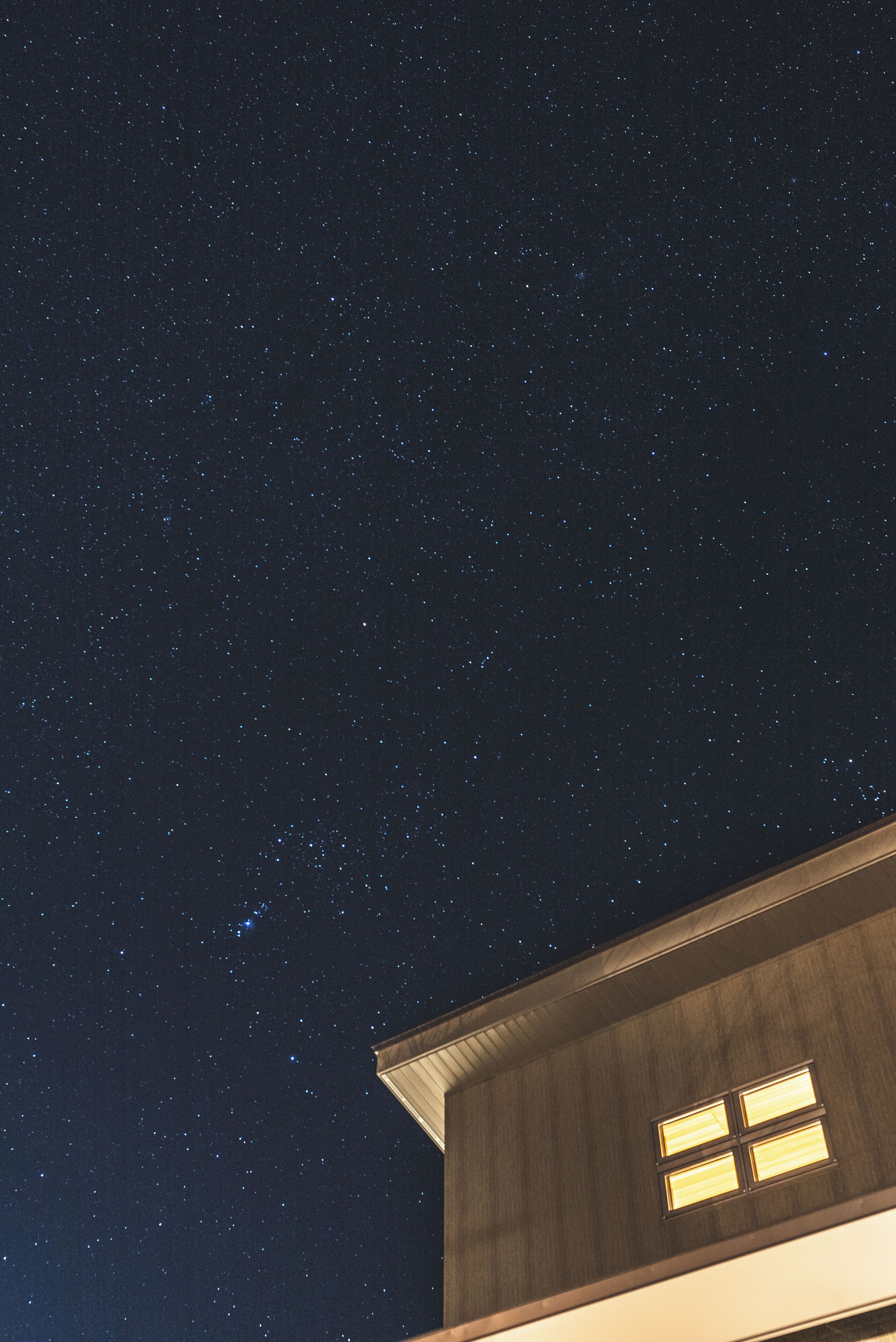 Cielo notturno stellato sopra un edificio con una finestra visibile.
