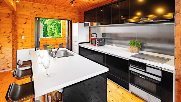A modern kitchen with a white countertop, stainless steel appliances, and wooden flooring. - Wadano Woods Chalet (Hakuba)