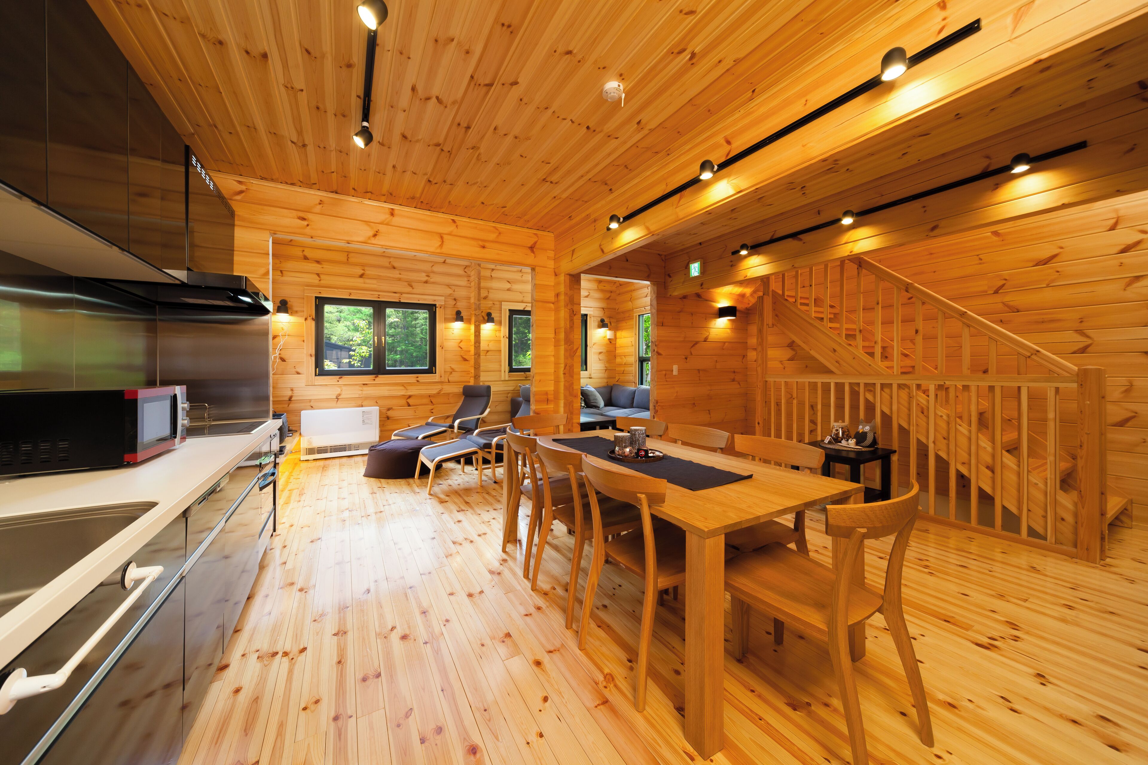 A wooden cabin interior with a kitchen, dining area, and a staircase.