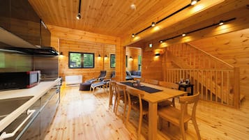 A wooden cabin interior with a kitchen, dining area, and a staircase.
