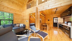 A wooden cabin interior with a sofa, armchairs, a dining table, and a kitchen area. - Wadano Woods Chalet (Hakuba)