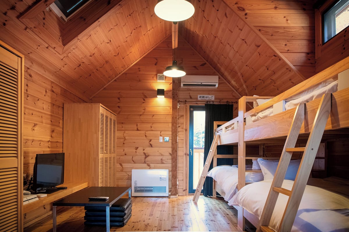 A wooden cabin with bunk beds, a desk with a computer, and an air conditioning unit.
