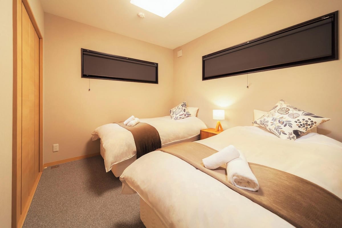 A hotel room with two beds, a flat-screen TV on the wall, a bedside table with a lamp, and a towel on each bed.