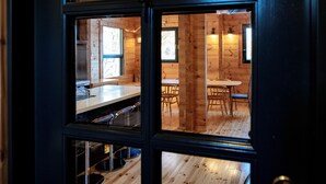 A view through a window of a wooden interior with a dining area, a sink, and a chair. - Wadano Woods Chalet (Hakuba)