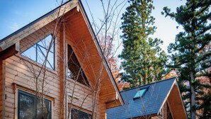 A wooden cabin with a steeply pitched roof, large windows, and a view of surrounding trees. - Wadano Woods Chalet (Hakuba)