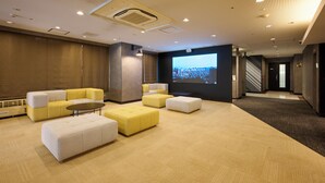 A modern hotel lobby with a large screen displaying the hotel name, plush seating areas, and a staircase leading to other floors. - JR WEST GROUP VIA INN SHINOSAKA (Osaka)