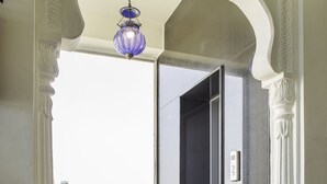 A hallway with a patterned floor, a blue hanging light, and a door with a number plate. - Kalyan Heritage (Jaipur)