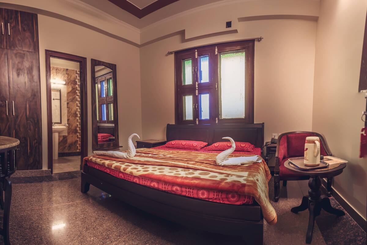 A spacious bedroom with a large bed, a sitting area with a chair and table, and a bathroom visible through an open door.