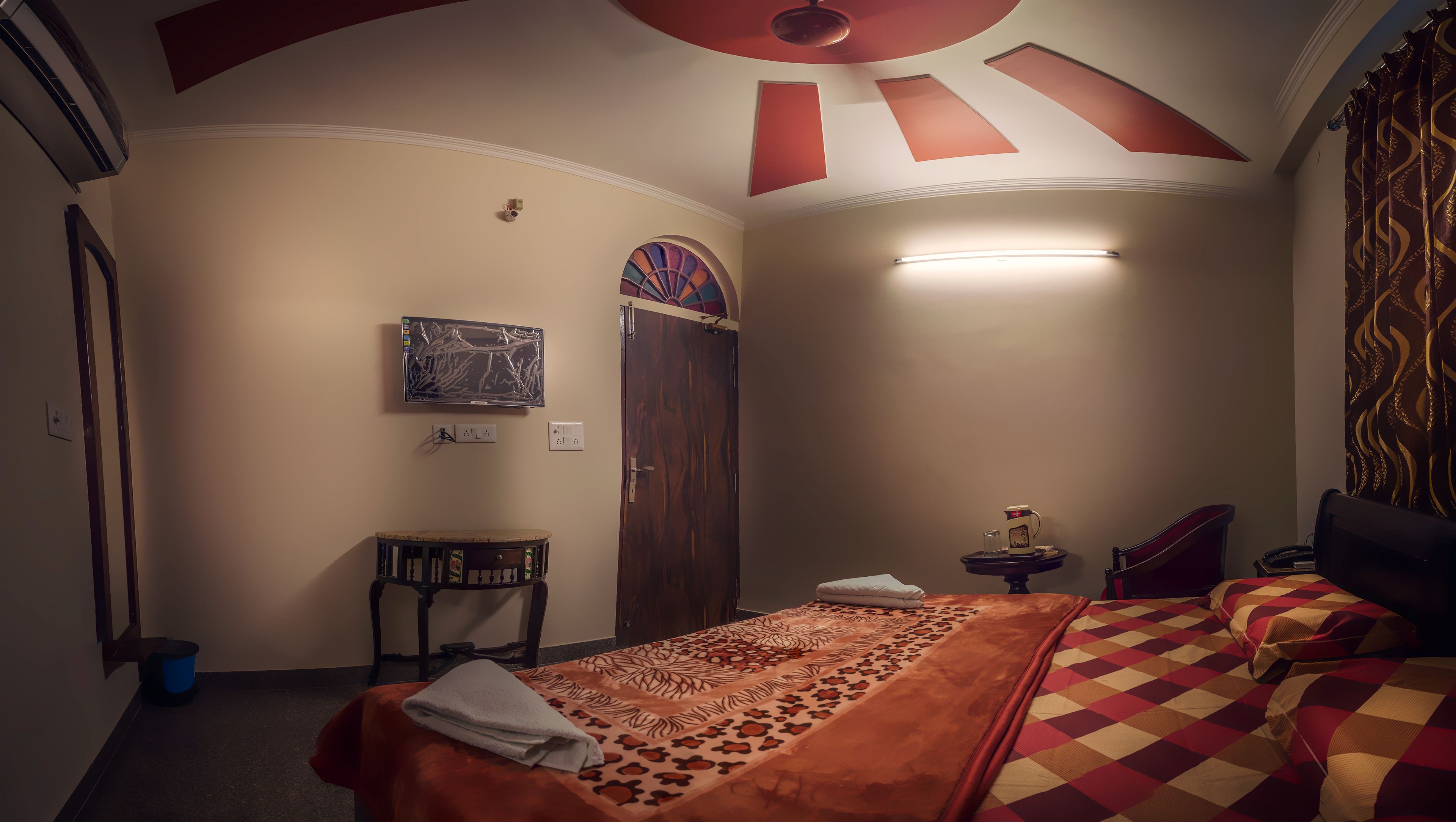 Ein Hotelzimmer mit einem Bett, einem kleinen Tisch, einem an der Wand befestigten Fernseher und einer Tür mit einem dekorativen Fenster.