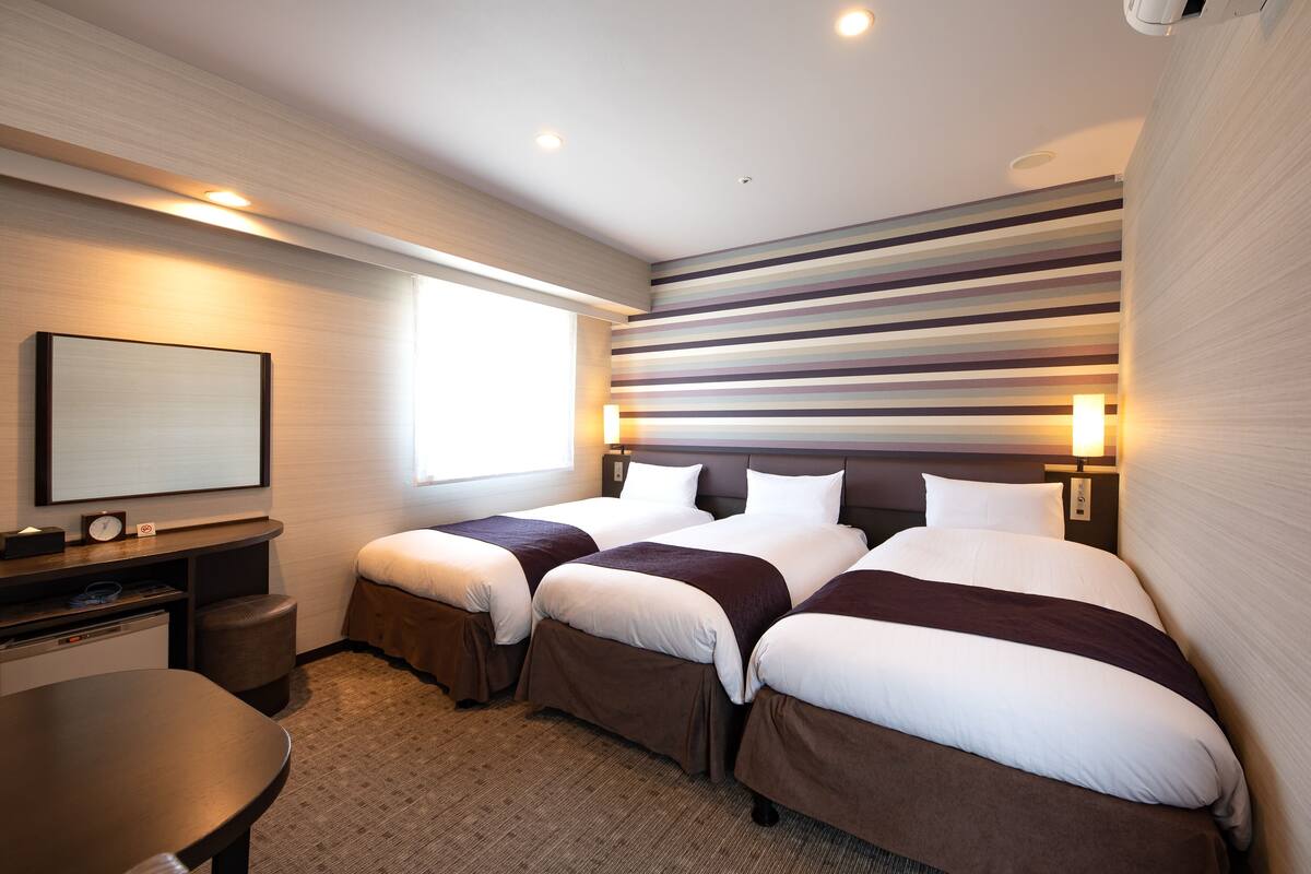 A hotel room with two beds, a desk, a chair, a TV, and a window.