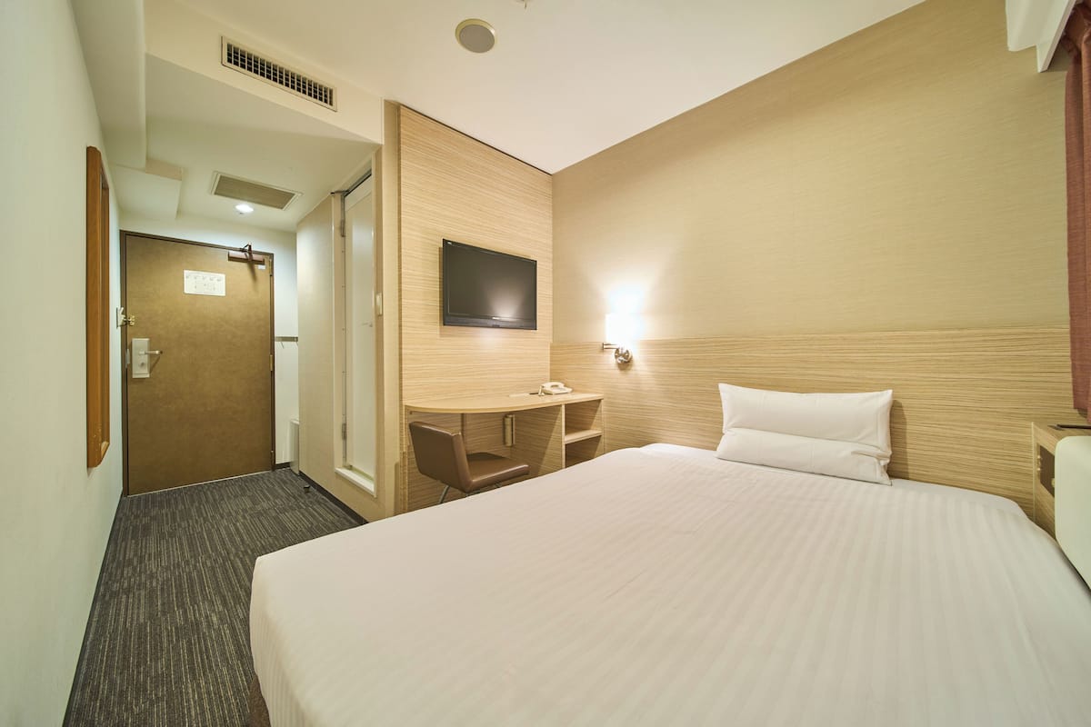 Camera d'albergo con un letto grande, una scrivania con una sedia, una TV a schermo piatto montata a parete e una porta che dà su un'altra stanza.