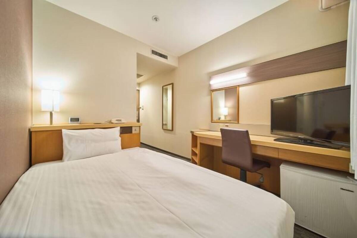 A hotel room with a bed, desk, chair, TV, and a mirror.
