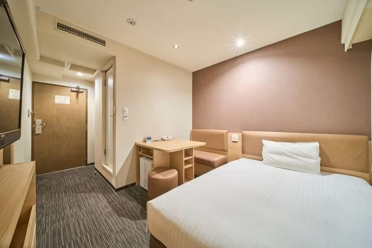 Una camera d'albergo con un letto, una scrivania, una sedia, una TV e una porta.