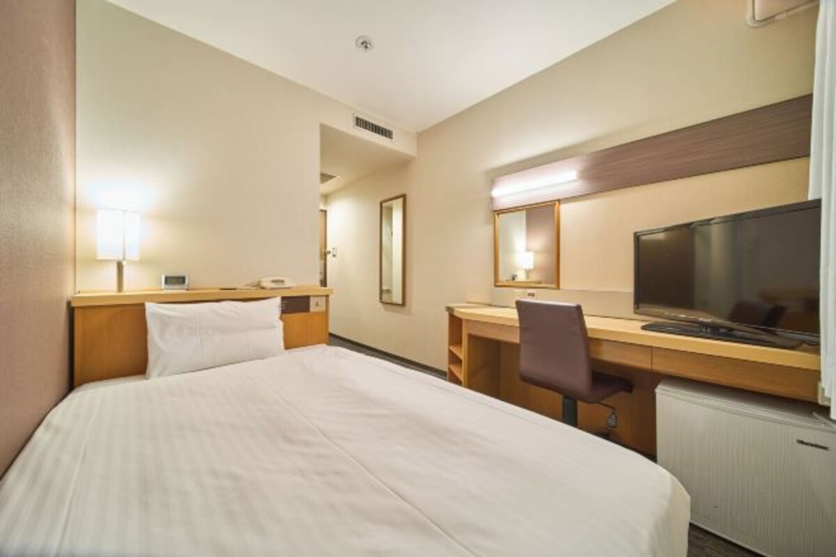Une chambre d’hôtel équipée d’un lit, d’un bureau, d’une chaise, d’une télévision et d’un miroir.