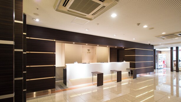 A modern reception area with a white counter, dark wood paneling, and a clean, tiled floor. - JR WEST GROUP VIA INN SHINOSAKA WEST (Osaka)